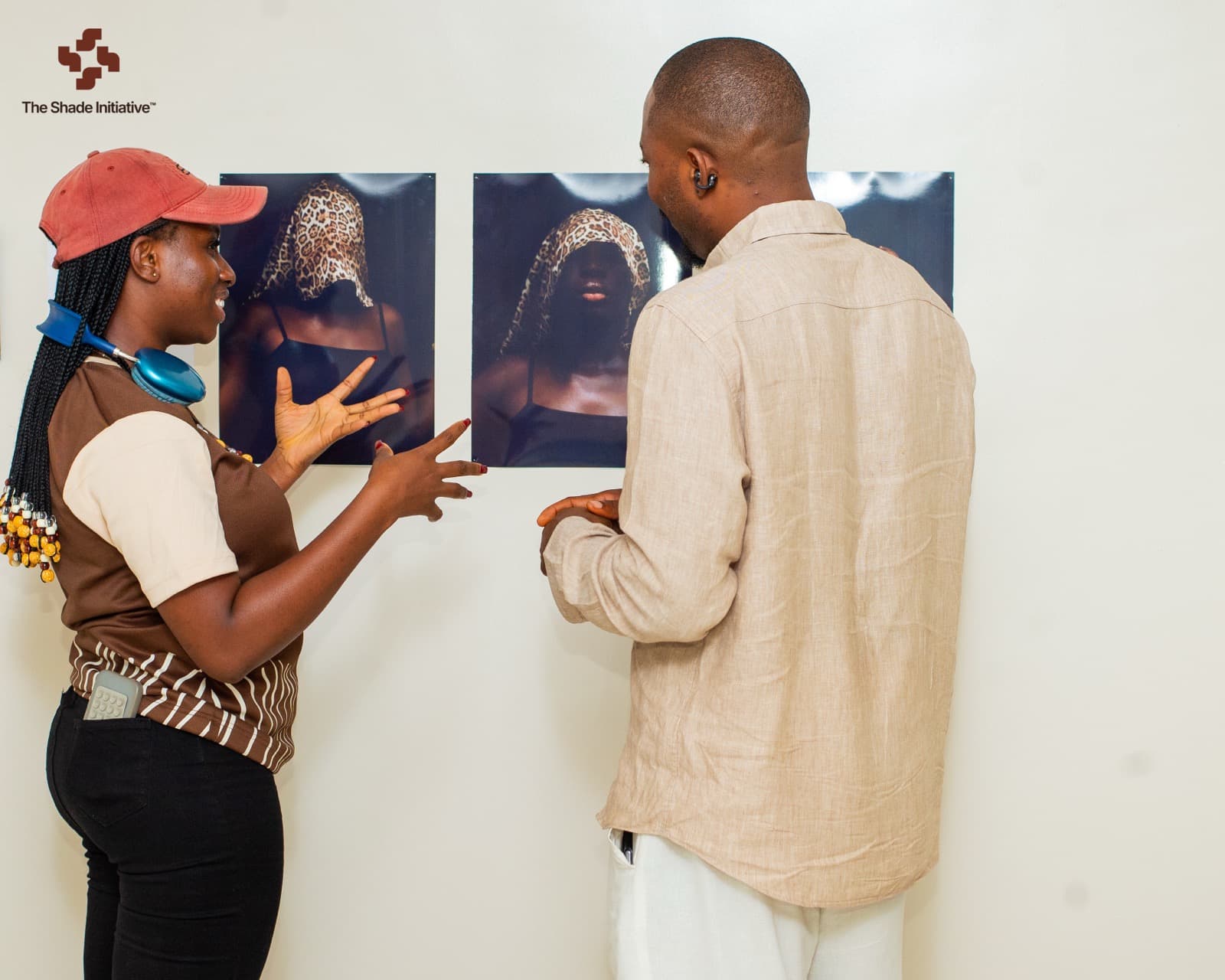 A participant gestures toward two hung prints as a guest studies them at the exhibition wall.
