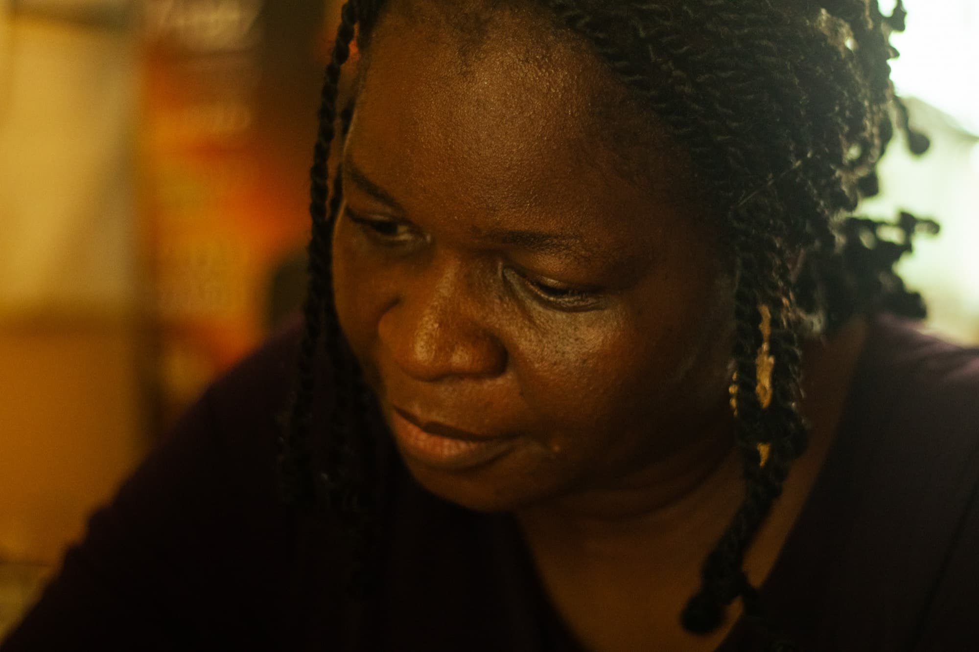 A warmly lit close up of a woman with braided hair looking down in a contemplative moment.
