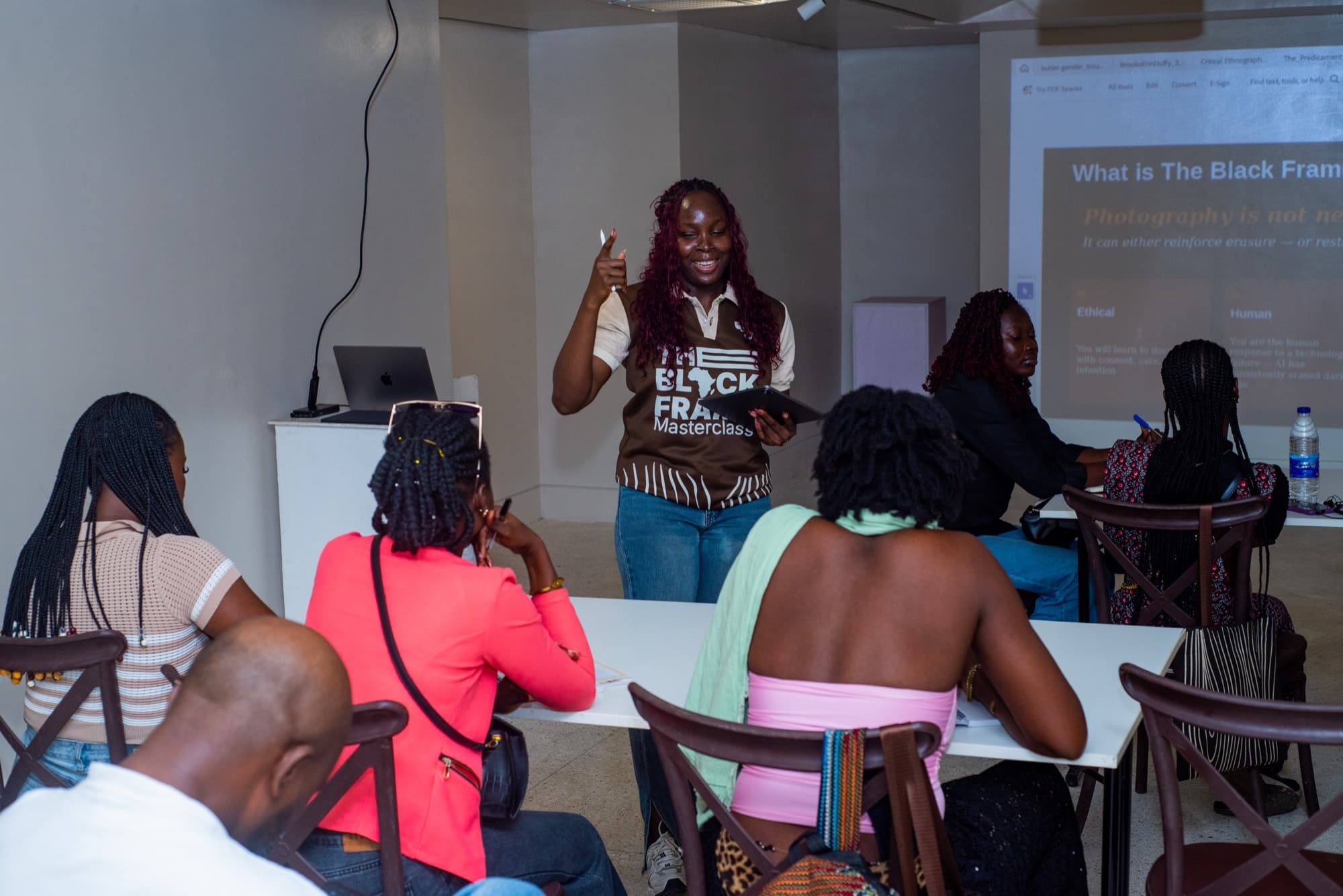 A facilitator gestures while speaking to participants, a slide behind her reading that photography is not neutral.