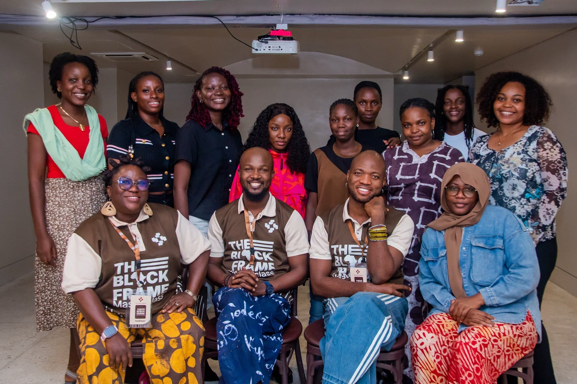 Group portrait of The Black Frame cohort standing behind three facilitators seated on stools, all smiling at the camera.