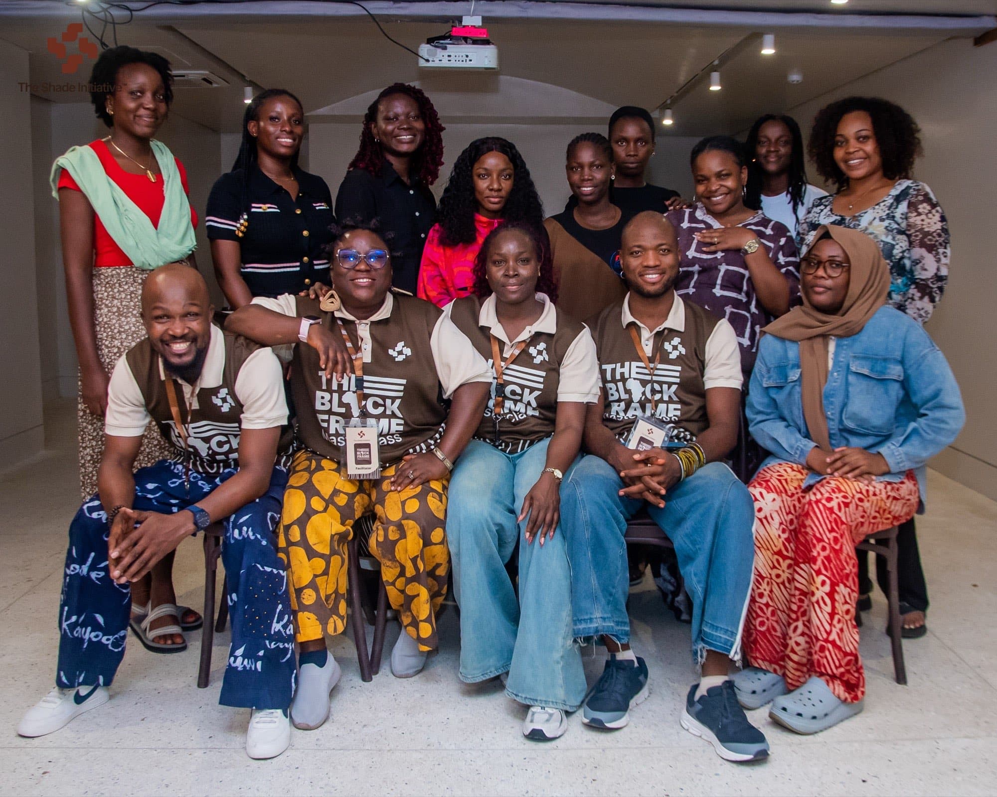 The Black Frame cohort, facilitators and team photographed together in the gallery at CCA Lagos, five of them seated at the front in Black Frame masterclass polo shirts.